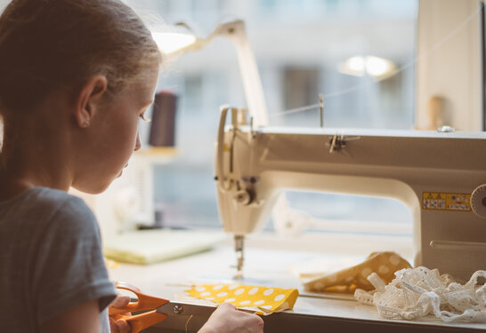 Little girl working on sewing machine at home.