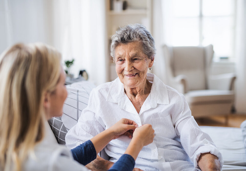 A health visitor helping a sick senior woman sitting on bed at home.