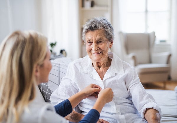 A health visitor helping a sick senior woman sitting on bed at home.