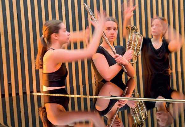 Performance d'élèves mêlant jeu de flûte traversière, bugle et gestes dansés dans une atmosphère scénique