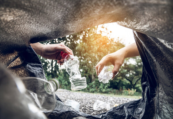 Deux mains déposent des bouteilles plastiques écrasées dans un sac poubelle noir, prise de vue depuis l'intérieur du sac