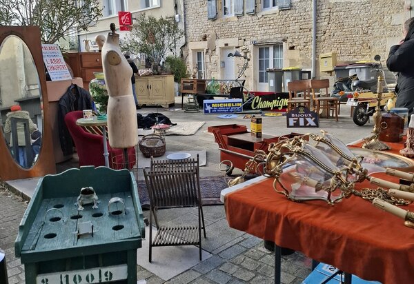 Meubles anciens, mannequin de couture, luminaires dorés et objets variés exposés en plein air sur un sol pavé