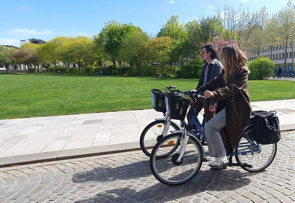 Un homme et une femme circulant à vélo sur une esplanade pavée bordée de pelouses verdoyantes par beau temps