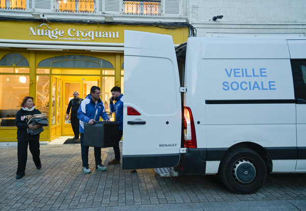 Agents en veste bleue chargeant des conteneurs repas dans le véhicule Veille Sociale du CCAS, en soirée
