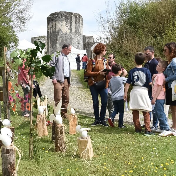 Familles avec enfants réunis devant la tour médiévale, décors d'œufs blancs posés sur des rondins de bois au premier plan