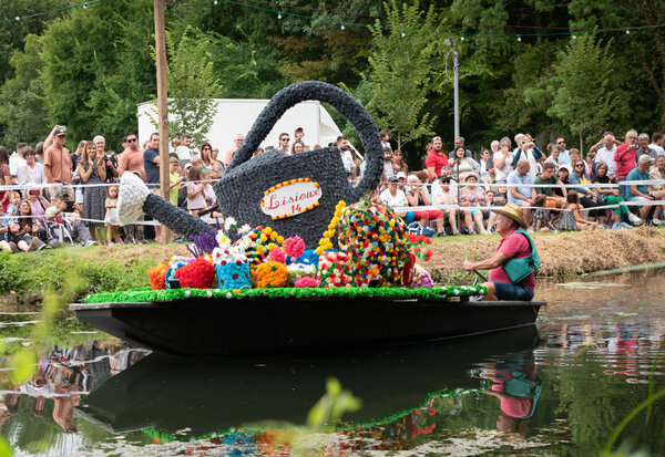 Bateau fleuri décoré d'un arrosoir géant en fleurs défilant sur l'eau devant une foule de spectateurs