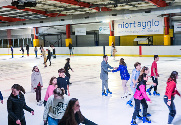 Patineurs de tous âges glissant sur la piste de glace de la patinoire de Niort Agglo lors d'une soirée disco.