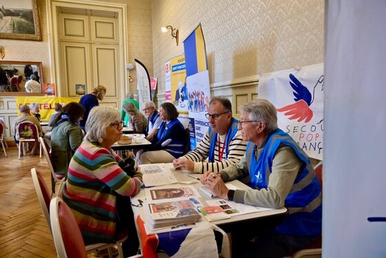 Bénévoles du Secours Populaire en gilets bleus échangeant avec une visiteuse au milieu des stands d'associations