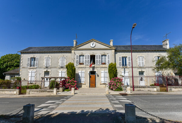 Façade de la mairie de la Foye Monjault en pierre de taille avec horloge centrale, volets blancs, drapeau tricolore et rosiers fleuris en façade
