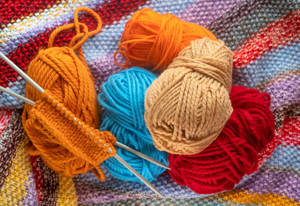 Pelotes de laine orange, bleue, beige et rouge posées avec des aiguilles à tricoter sur un tissu coloré