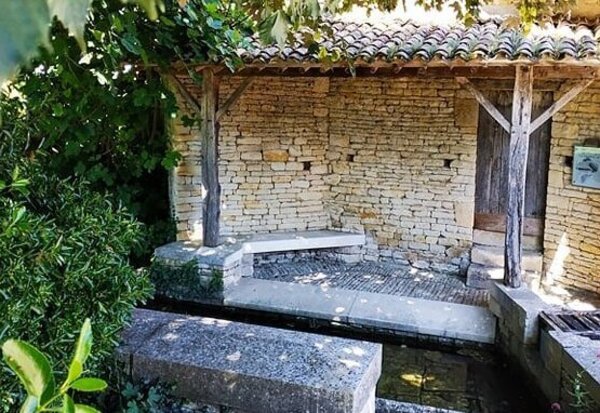 Lavoir en pierre couvert d'un auvent de tuiles, entouré de végétation, typique du patrimoine rural maraîchin