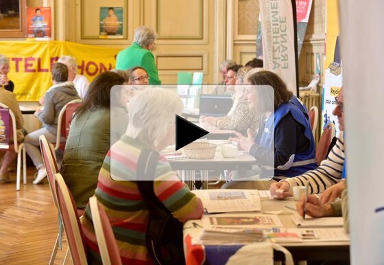 Visiteurs et représentants d'associations, dont Alzheimer France et le Téléthon, échangent autour de tables dans la grande salle.