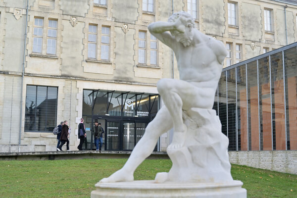 Statue en marbre blanc d'un homme en mouvement au premier plan devant l'entrée des Musées Bernard d'Agesci