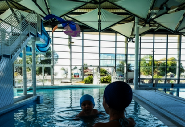 Adultes accompagnant de jeunes enfants dans le bassin d'une piscine couverte, avec des jouets aquatiques colorés