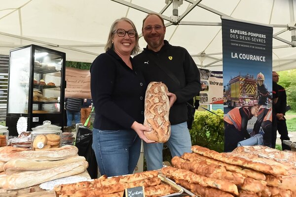 Deux producteurs présentant un pain artisanal devant un étal garni de pains et viennoiseries locaux