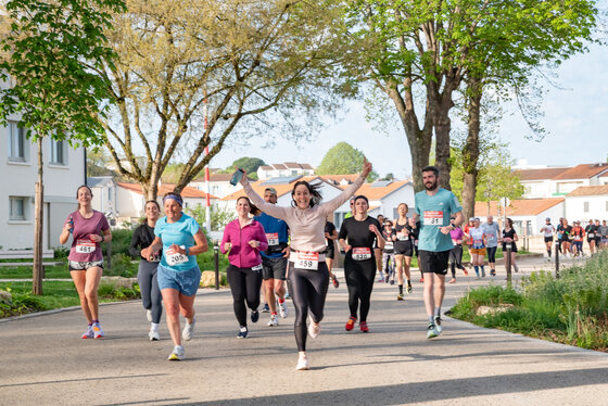 Groupe de coureurs avec dossards sur un chemin arboré, une participante bras levés exprimant sa joie