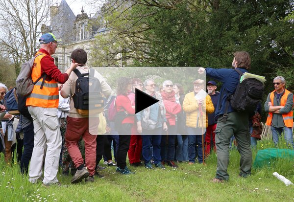 Participants rassemblés autour d'animateurs en gilet orange lors d'une balade commentée en extérieur, château de chanterelle en arrière-plan