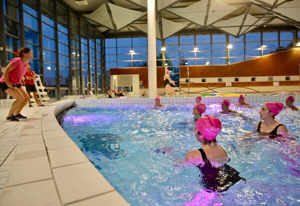 Animatrice sur le bord du bassin dirigeant des participantes lors d'une séance collective d'aquagym en soirée