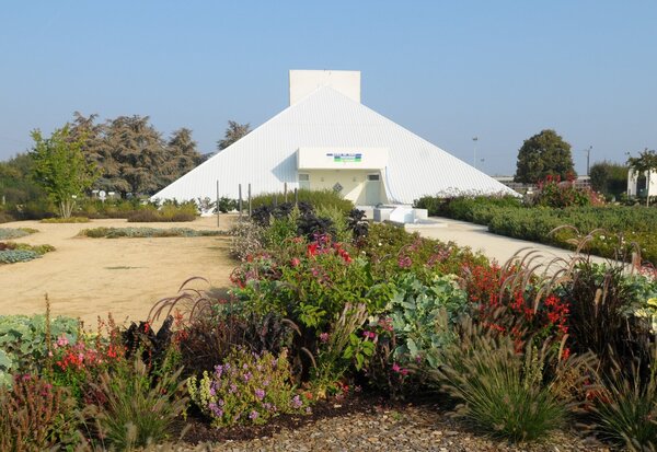 Bâtiment à toiture pyramidale blanche entouré de massifs fleuris aux plantations variées et colorées