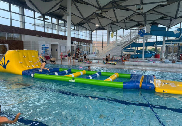 Parcours d'obstacles gonflables multicolores flottant dans le bassin intérieur de la piscine, avec des participants en action