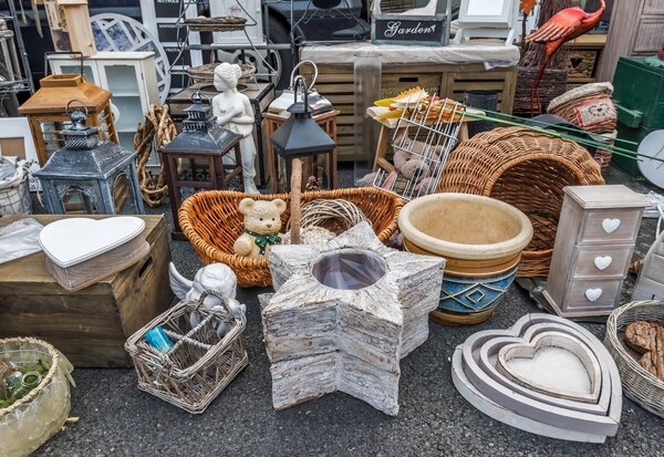 Articles de seconde main exposés au sol : paniers tressés, lanternes, bibelots, pots en céramique et boîtes décoratives.