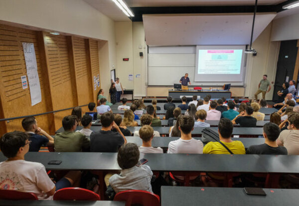Amphithéâtre universitaire bondé d'étudiants suivant une présentation projetée sur écran