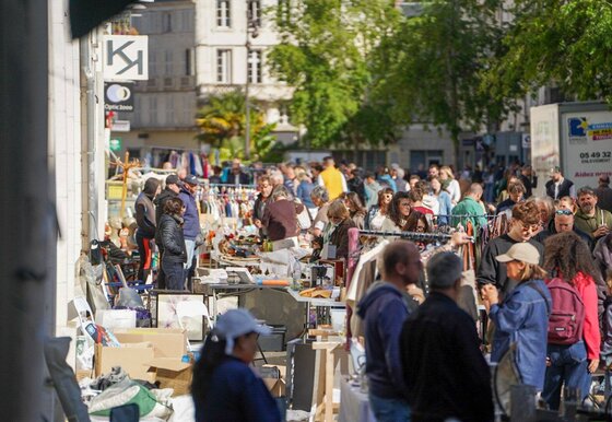 Stands couverts d'objets et vêtements sur portants installés en plein air le long d'une rue ensoleillée du centre-ville de Niort