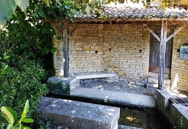 Lavoir en pierre couvert d'un auvent de tuiles, entouré de végétation, typique du patrimoine rural maraîchin
