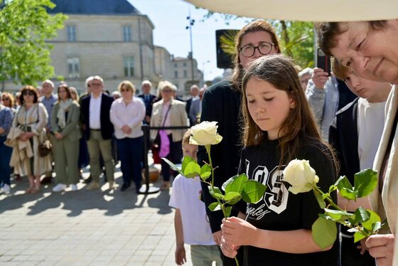 Une fillette et une femme tiennent des roses blanches en signe d'hommage, entourées d'une foule recueillie.