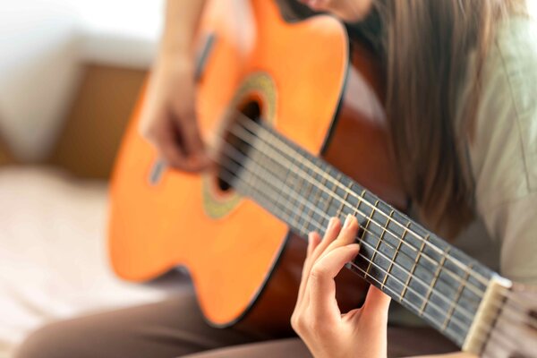 Gros plan sur les mains d'une jeune guitariste pinçant les cordes d'une guitare classique acoustique