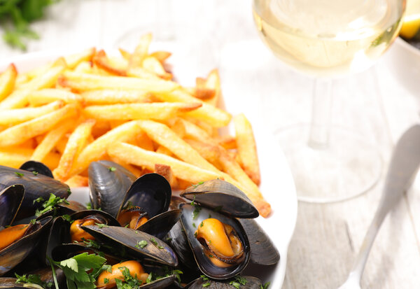Assiette de moules marinières garnies de persil, accompagnées de frites dorées et d'un verre de vin blanc