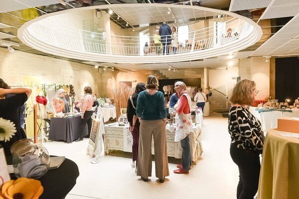 Visiteurs découvrant les stands d'artisans dans une grande salle dotée d'un balcon circulaire
