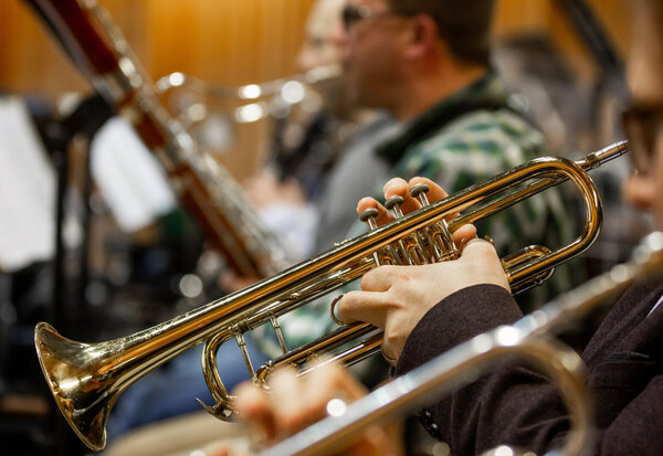 Mains d'un musicien tenant une trompette dorée, d'autres instrumentistes visibles en arrière-plan flou