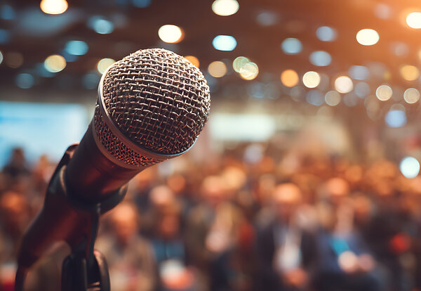 Microphone au premier plan devant une salle remplie de participants lors d'une prise de parole en public