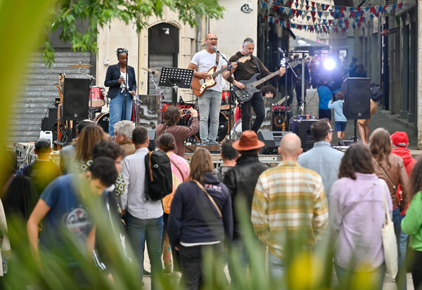 Concert en plein air dans une rue : guitaristes sur scène face à un public nombreux sous des guirlandes tricolores