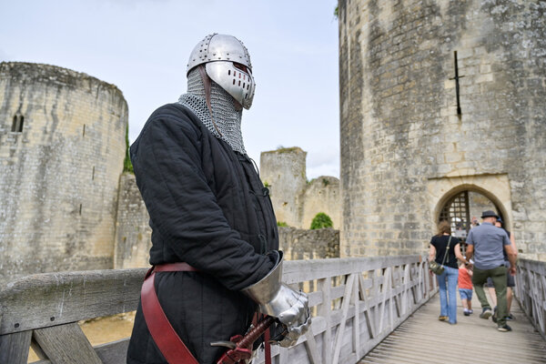 Animateur costumé en chevalier médiéval, heaume et gantelet, sur le pont d'accès au château, visiteurs en arrière-plan