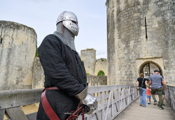 Animateur costumé en chevalier médiéval, heaume et gantelet, sur le pont d'accès au château, visiteurs en arrière-plan