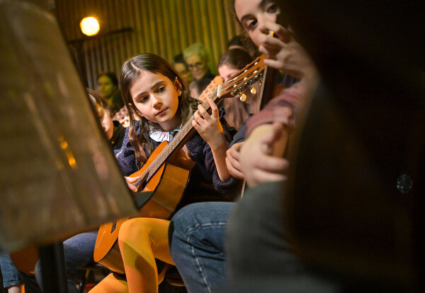 Jeunes élèves jouant de la guitare classique en groupe lors d'un concert, pupitre à partitions au premier plan