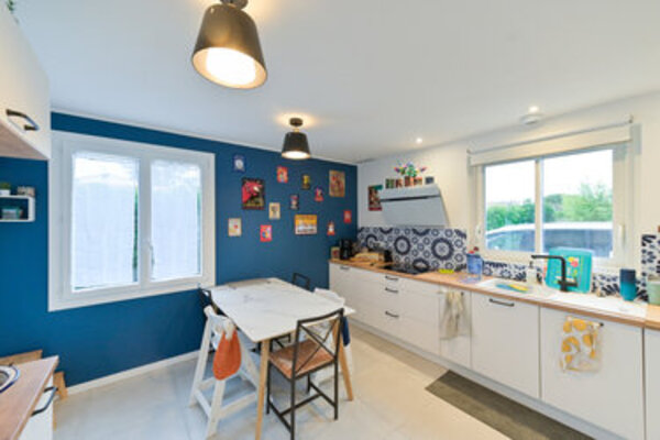 Intérieur d'une cuisine-séjour moderne avec mur bleu, plan de travail en bois et luminosité naturelle