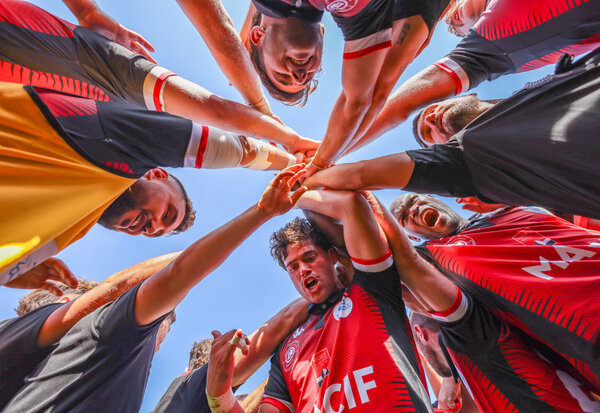 Rugbymen en cercle, mains jointes au centre, rassemblement d'équipe en maillot rouge et noir avant une rencontre