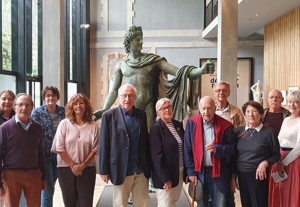 Groupe de membres de l'association réunis dans le hall du musée devant une grande statue antique en bronze