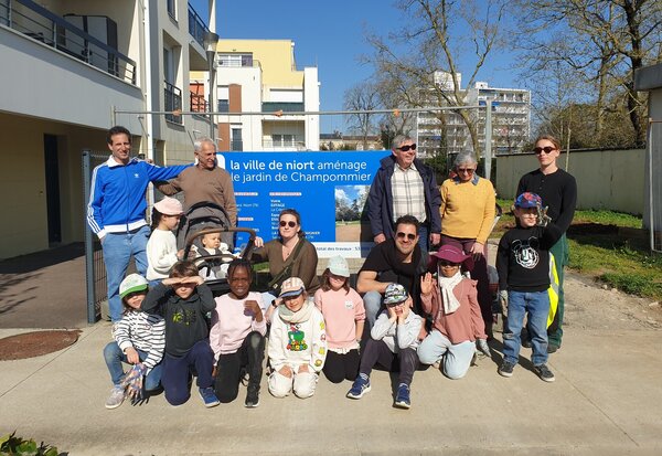 Groupe d'habitants adultes et enfants rassemblés devant le panneau de chantier du jardin de Champommier